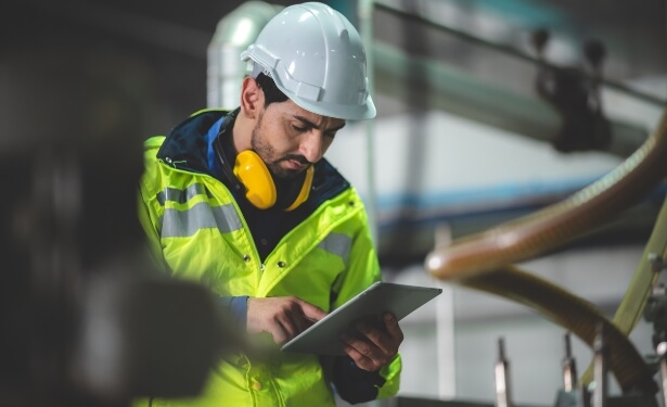 a man in reflective jacket and white hard hat looking at a tablet device